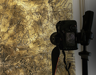 A digital camera photographing an antique art piece resembling the signed wall of a cave.