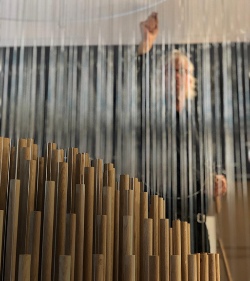 The artist finalising their piece. It is a handing sphere made from hanging wooden rods.